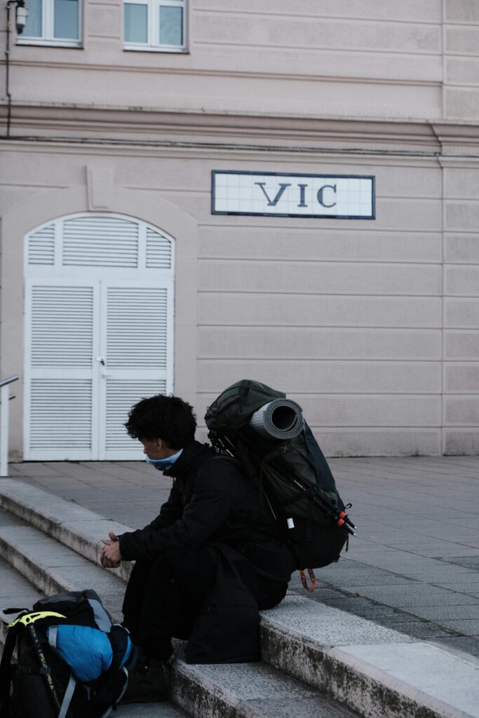 A solitary backpacker sits outside a building marked 'Vic', taking a break.